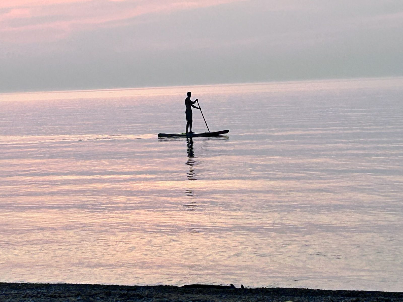 A lone paddleboarder silhouetted on completely flat Lake Huron water at sunset