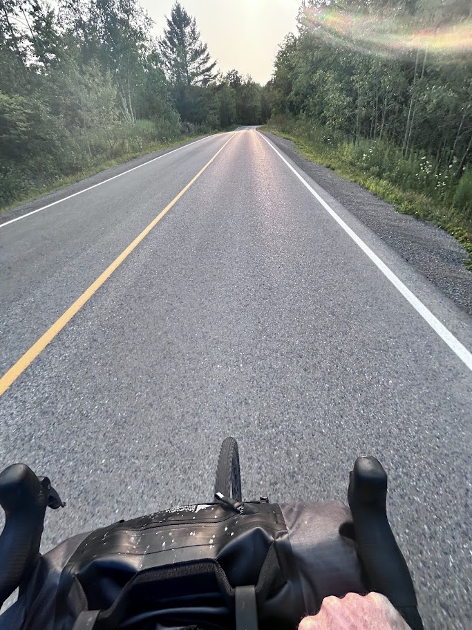 A paved road at dusk on the final approach to Kasshabog Lake, seen from the handlebars