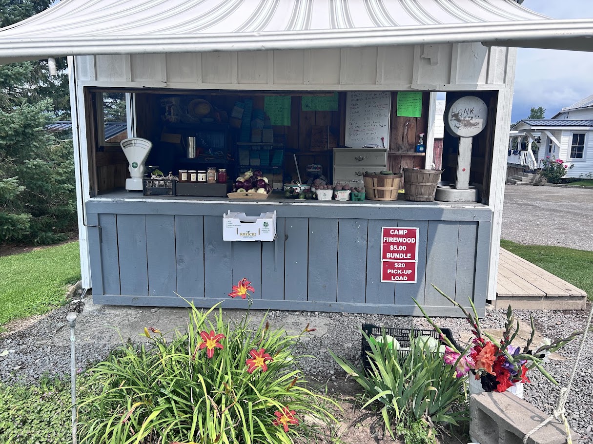 An honesty-system farm stand with produce, firewood for sale, and a honk sign